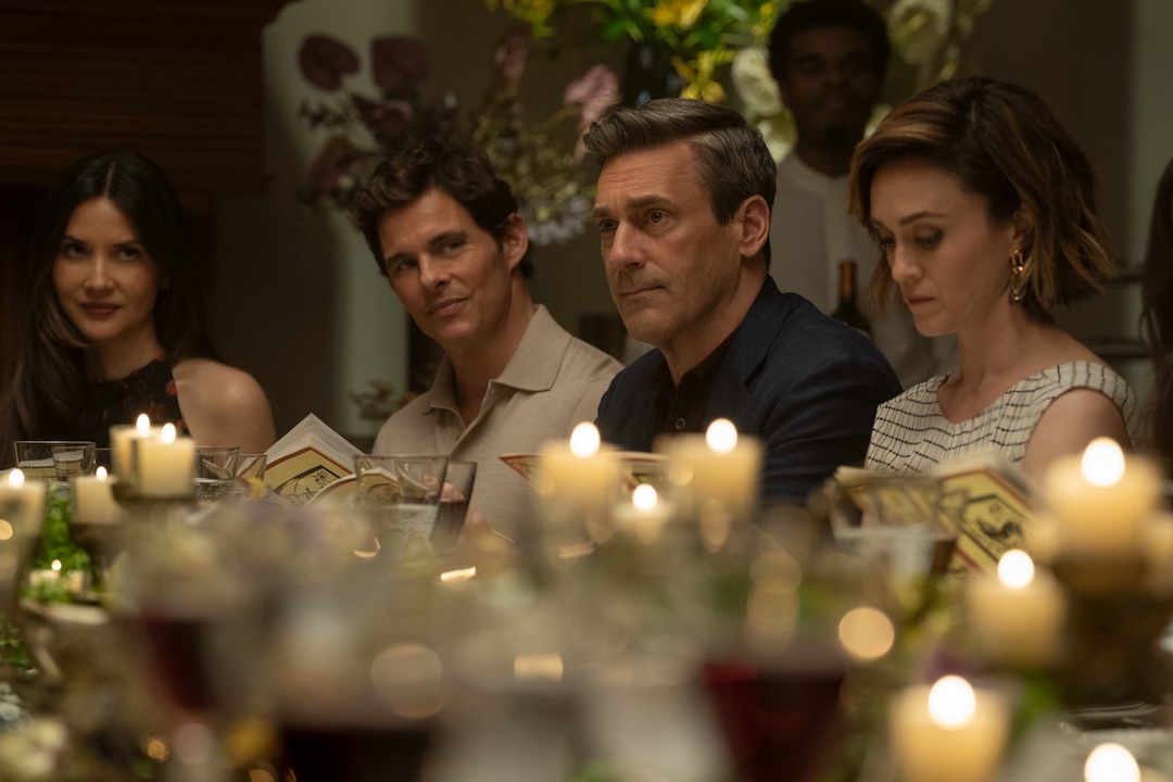 Jon Hamm, as Coop, is seating at a fancy-looking dinner table with candles and glasses of wine, along with other guests, including James Marsden, as the new neighbor, and Olivia Munn, as Sam.