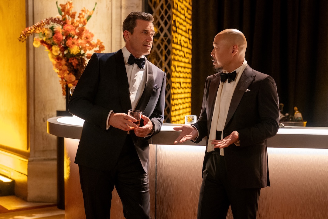 Jon Hamm, as Coop, and Hoon Lee, as Barney Choi, are chatting at the bar at a black tie event. Barney looks upset.
