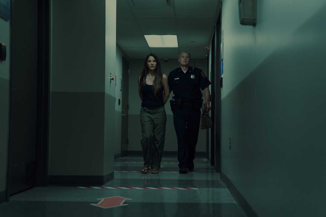 Olivia Munn, as Sam, is being escorted, handcuffed, by a police officer down a corridor.