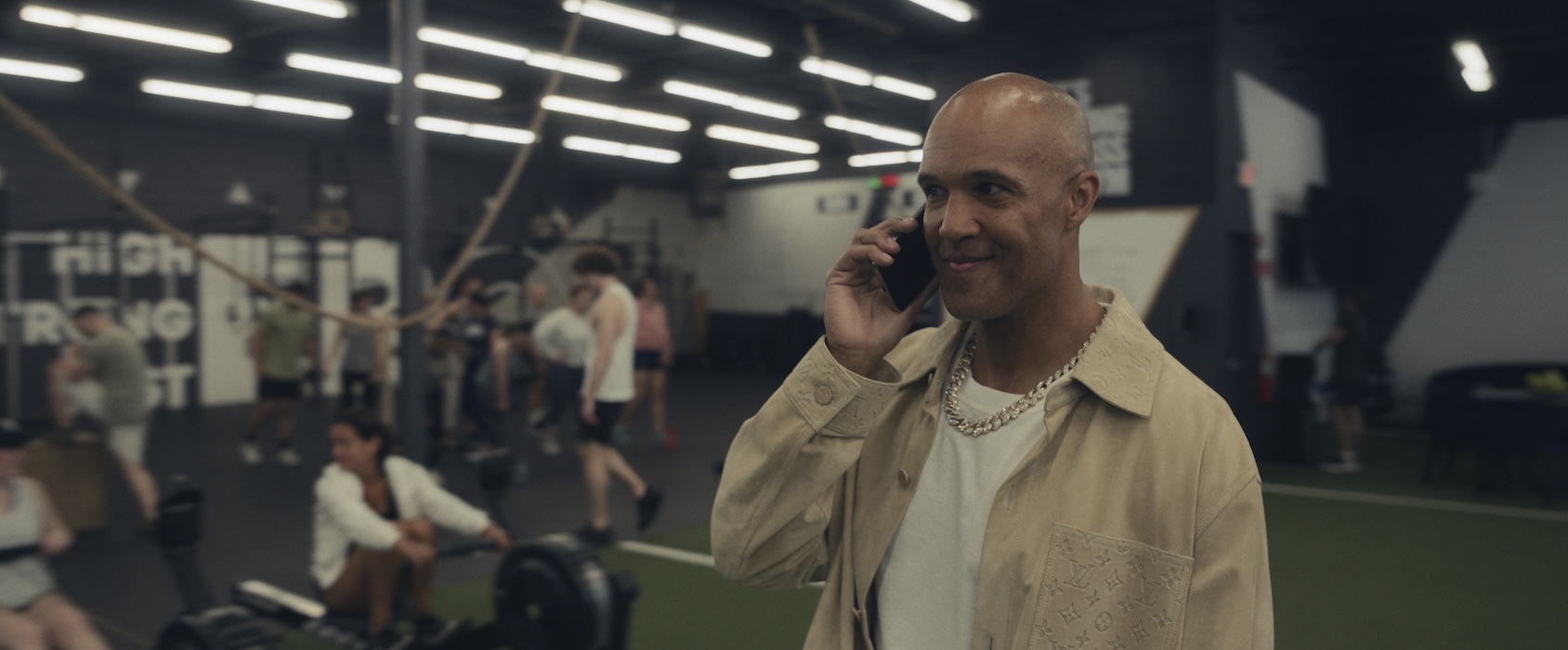 Mark Tallman, as Nick, is on the phone in a gym, looking content.