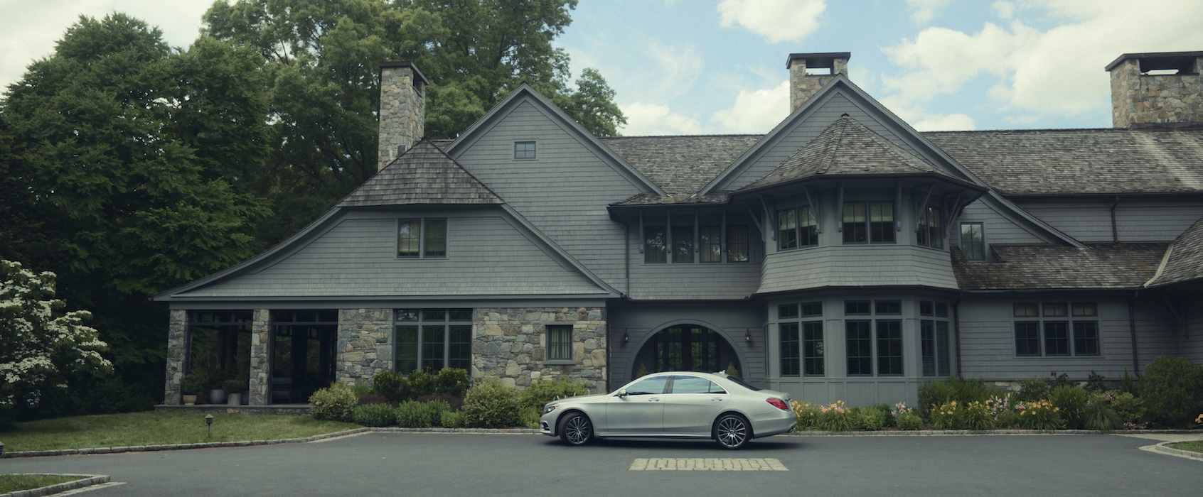 A fancy mansion with a metal gray luxury sedan parked in front of it.