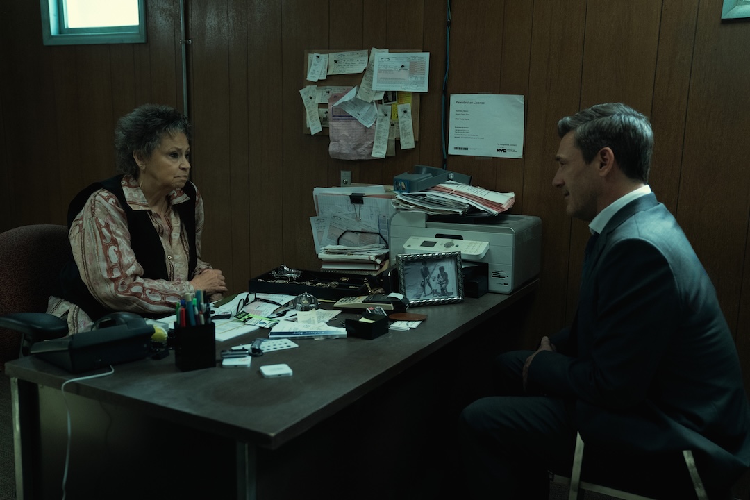 Jon Hamm, as Coop, is sitting in the back office of a pawn shop with its owner, seemingly in the middle of a negotiation.
