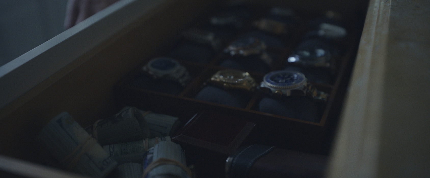 A drawer full of luxury watches and rolls of cash.